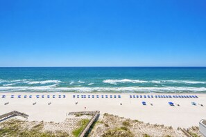 Una playa con hileras de sombrillas azules y sillones blancos.