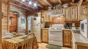 A cozy cabin-style kitchen with wooden cabinets, a refrigerator, stove, and a dining area with a table set for four.
