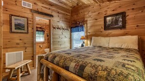 A cozy cabin bedroom with a wooden bed, a bench, and a rustic decor including a sign that reads "Always Kiss Me Goodnight".