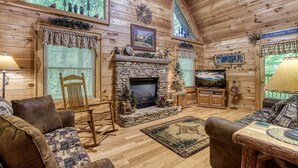 A cozy log cabin interior with a stone fireplace, wooden furniture, and a television.