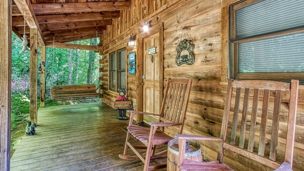 A wooden cabin with a porch, rocking chairs, and a bear decoration.