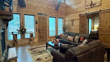 A rustic cabin interior with a wooden interior, a leather sofa, a fireplace, and mounted animal heads.