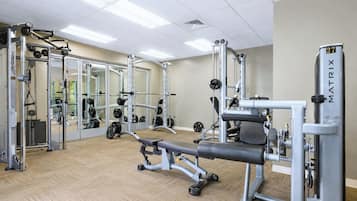 A gym with weightlifting equipment, mirrors, and a wooden floor.