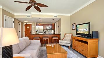 A living room with a sofa, coffee table, TV, and a kitchen area in the background.
