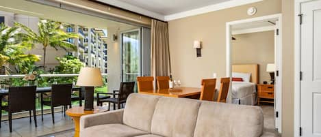 Una habitación de hotel moderna con sofá, mesa de comedor, sillas y un balcón con vistas a palmeras y un edificio.