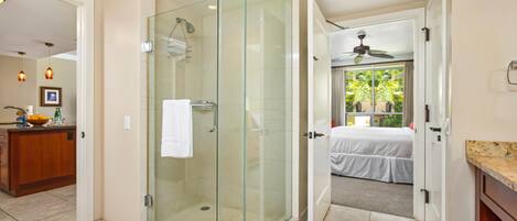 Un baño moderno con ducha envuelta en vidrio, un perchero a la vista y una cama en la habitación contigua.