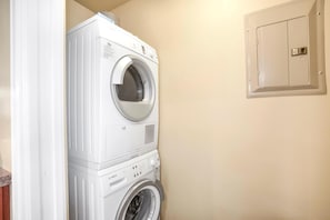 Une machine à laver et un sèche-linge superposés dans une buanderie, avec un mur de couleur beige et un meuble utilitaire.