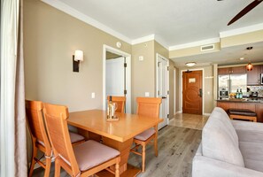 Un coin repas avec une table et des chaises en bois, une cuisine à l’arrière-plan et un salon avec un canapé.