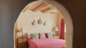 Un dormitorio con techo de madera, una cama con falda floral, dos mesitas de noche con lámparas y una alfombra pequeña en el suelo.