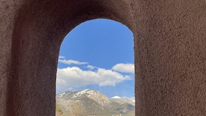 Vista a través de un ventanal arqueado de un edificio, con un paisaje montañoso al fondo.