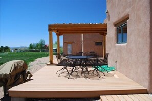 Een terras buiten met een houten terras, een ronde tafel met stoelen, en een pergola.