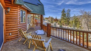 A log cabin with a wooden deck, outdoor seating, and solar panels on the roof. - Golden Oak Estate by Destination Big Bear : Luxury Log Home in Castle Glen! Walk to the Lake! Beautiful Mountain Views! (Big Bear Lake)