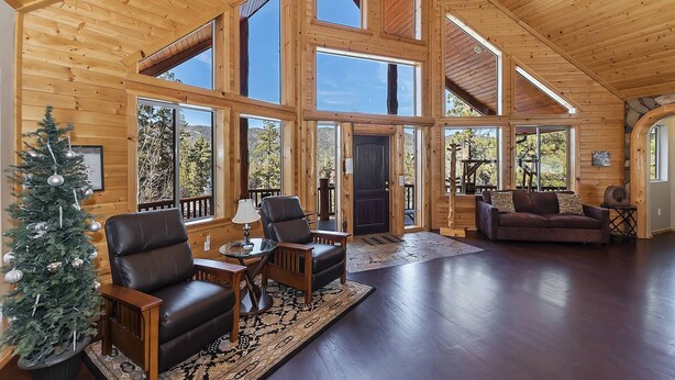 A spacious wooden interior with large windows, a fireplace, and a Christmas tree. - Golden Oak Estate by Destination Big Bear : Luxury Log Home in Castle Glen! Walk to the Lake! Beautiful Mountain Views! (Big Bear Lake)