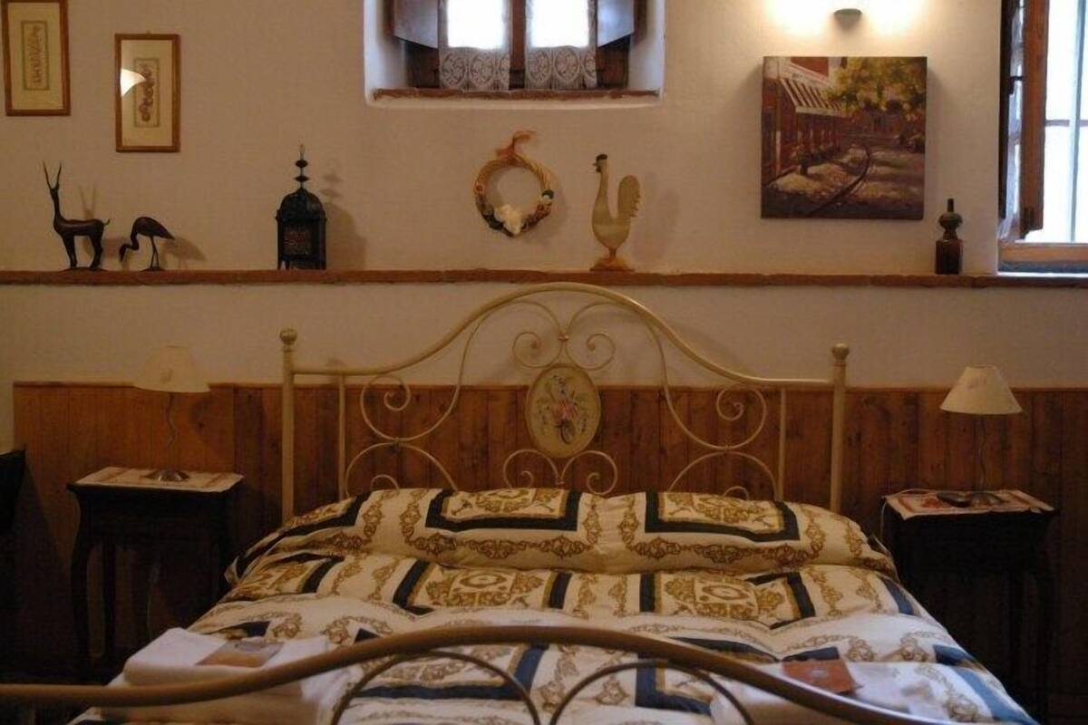 A bed with a decorative headboard, a wooden headboard, a bedside table with a lamp, and a window with curtains.