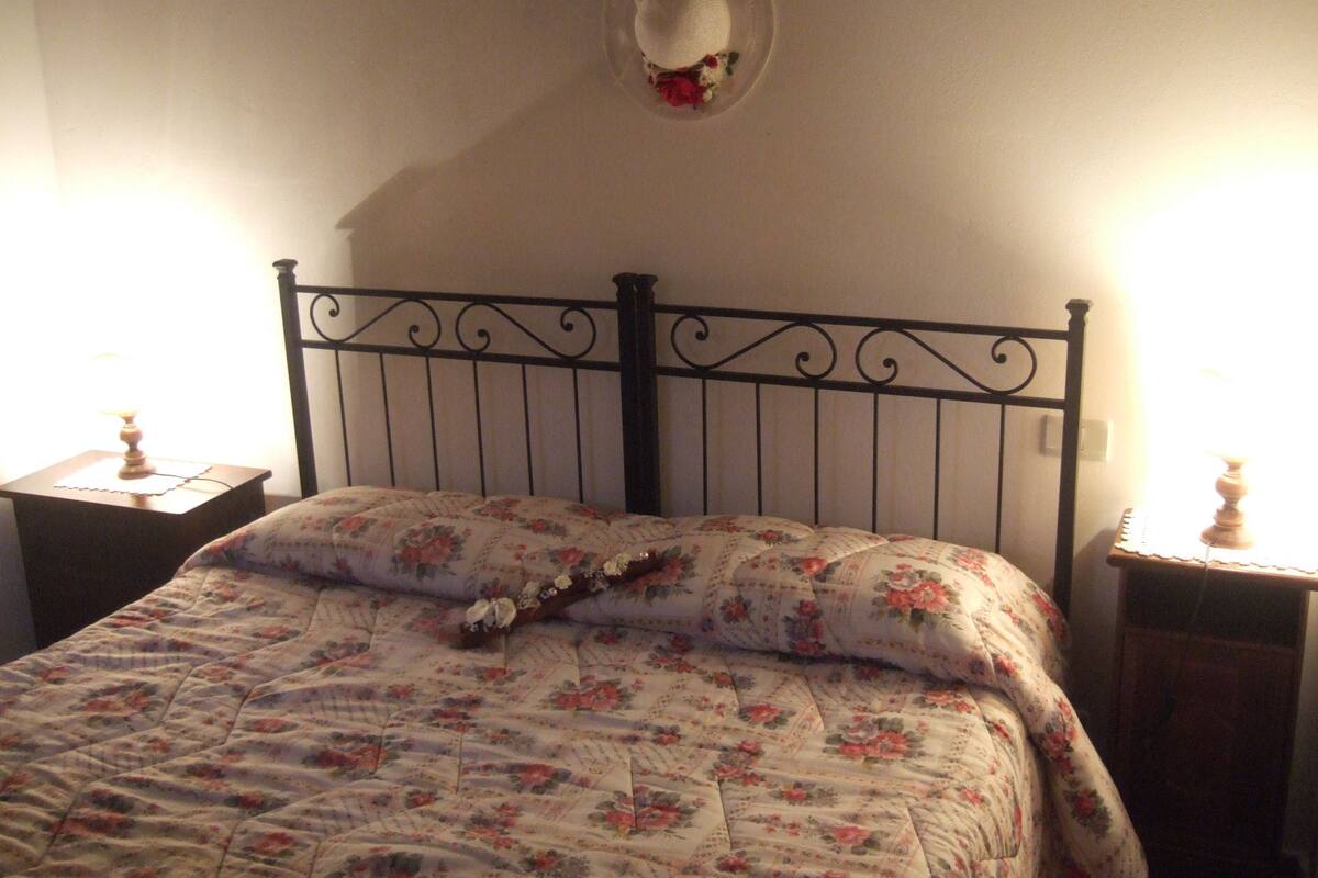 A bed with a floral quilt, a decorative wall hanging, and two bedside lamps.
