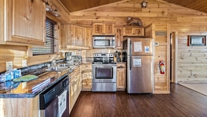 A wooden cabin kitchen with a stove, microwave, refrigerator, and wooden cabinets. - Love Me Tender: Amazing Views, Romantic, Fire Pit (Gatlinburg)