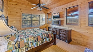 A wooden cabin bedroom with a bed, dresser, TV, and windows. - Love Me Tender: Amazing Views, Romantic, Fire Pit (Gatlinburg)
