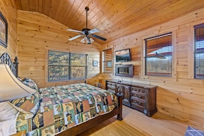 A wooden cabin bedroom with a bed, dresser, TV, and windows. - Love Me Tender: Amazing Views, Romantic, Fire Pit (Gatlinburg)
