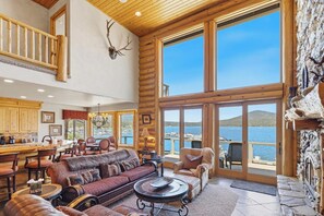 A spacious living area with a large window overlooking a body of water, a fireplace, and a kitchen area.