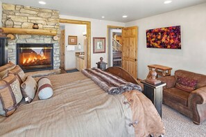 Ein Schlafzimmer mit Kamin aus Stein, einem Bett mit vielen Kissen, einer Holztür und einem Bild an der Wand.