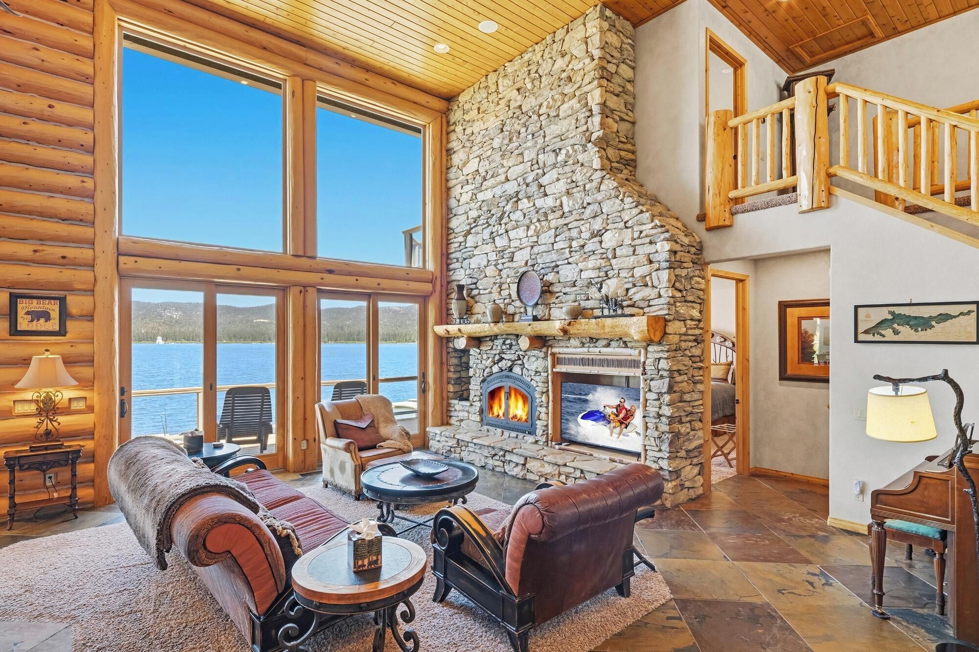 A log cabin interior with a stone fireplace, leather sofas, and a view of a lake.