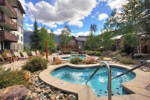 A resort with a pool area, lounge chairs, and a mountainous backdrop. - Beautiful Passage Point Condo. Two blocks to American Eagle and American Flyer lifts. (Copper Mountain)