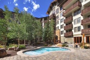Relax by the pool surrounded by lush greenery and trees, with a modern hotel building in the background.