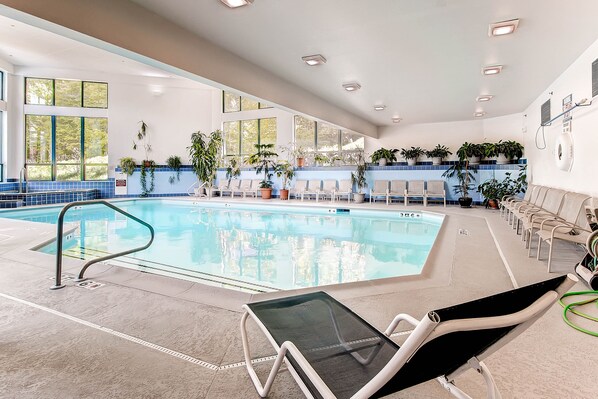 An indoor swimming pool with clear water, surrounded by lounge chairs and potted plants.