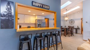 A kitchen area with a bar counter, bar stools, and a 'HAPPY HOUR' sign. - AWBR04 - Walk to Fort Rock, Single Level, Hot Tub, Bikes, BBQ (Sunriver)