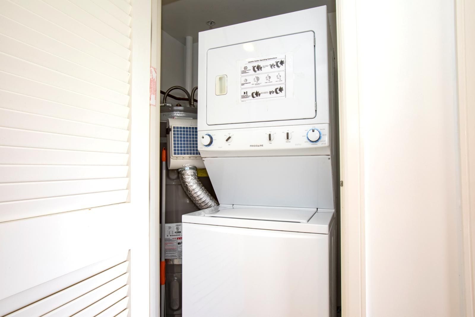 A compact laundry room with a front-loading washer and dryer, a control panel with operating instructions, and a visible vent hose.