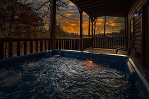 Ein Whirlpool auf einer Holzterrasse mit Blick auf einen Sonnenuntergang und Bäume im Hintergrund.