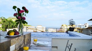A rooftop terrace with a swimming pool, dining setup with plates and cutlery, and a vase with flowers.