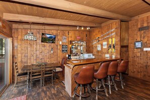 Ein Holzinterieur mit Barbereich, Barhocker, einem Fernseher und Skiausrüstung an den Wänden.