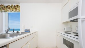 Une cuisine de taille réduite, dotée d’une fenêtre, d’un four à micro-ondes, d’un four traditionnel et d’un évier.