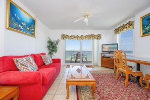 Sala de estar com sofá vermelho, mesa de centro de madeira, televisão e varanda com vista.