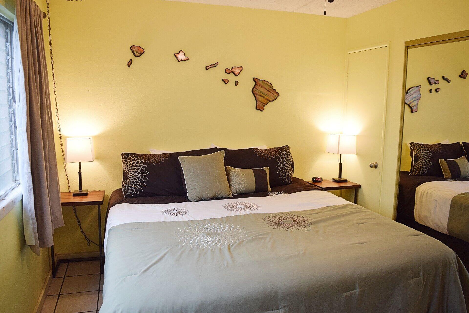 Una habitación de hotel con una cama, dos mesitas de noche con lámparas, un espejo y adornos en la pared.