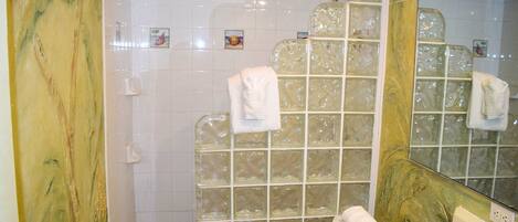 Un baño con cabina de ducha de vidrio, azulejos blancos y un espejo grande.