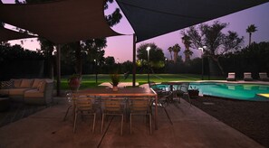 An outdoor patio area with a pool, a table with chairs, and a covered seating area.