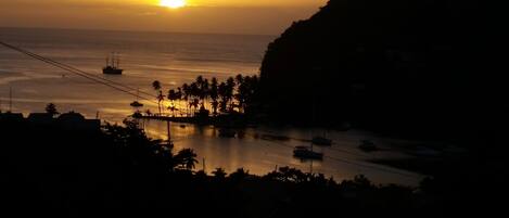 Un atardecer costero con barcos y palmeras.