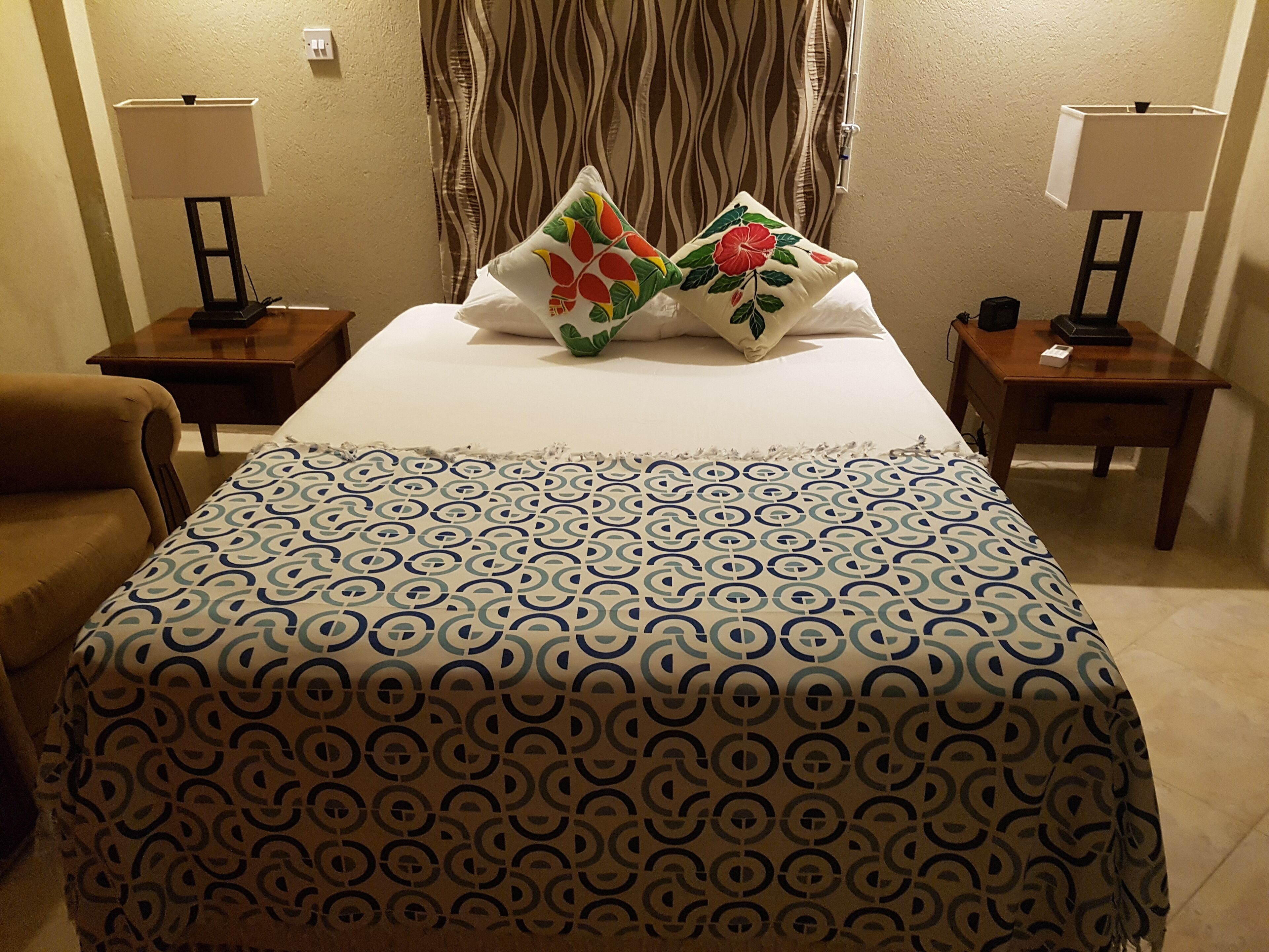 Een hotelkamer met een bed, twee nachtkastjes, een lamp op elk nachtkastje, een bed met een patroon en een bloemenkussen.