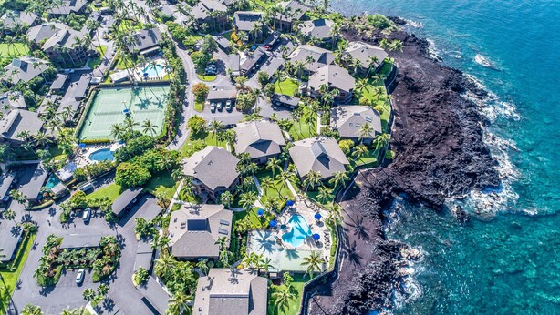 An aerial view of a coastal resort with multiple buildings, swimming pools, and lush greenery.