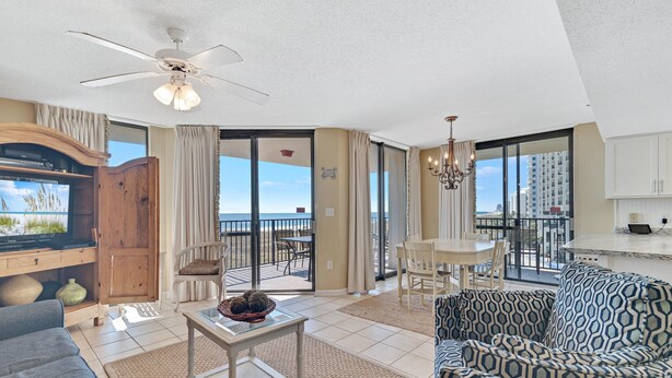 A spacious living room with a large TV, comfortable seating, a ceiling fan, and a balcony with a view of the ocean. - Phoenix VII 301 | Beachfront | Updated | Pools | My Beach Getaways (Orange Beach)