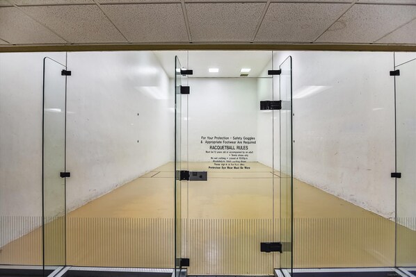 Una cancha de racquetball con puertas de vidrio y un letrero que detalla las normas de seguridad y los requisitos de edad.