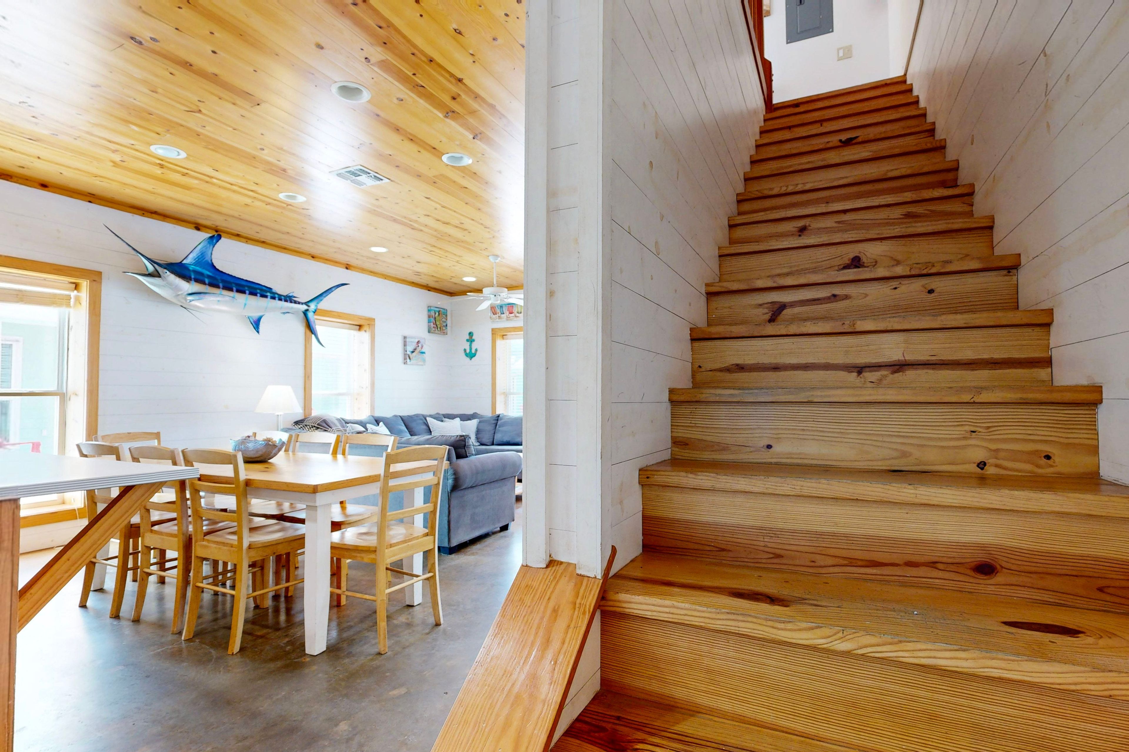 Eine Holztreppe führt zu einer oberen Ebene, einem Essbereich mit Tisch und Stühlen und einer blauen Fischdekoration an der Decke.