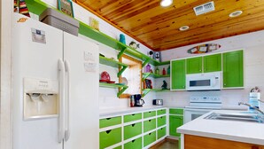 Eine Küche mit grünen Schränken, einem weißen Kühlschrank, einer Mikrowelle und einem Spülbecken.