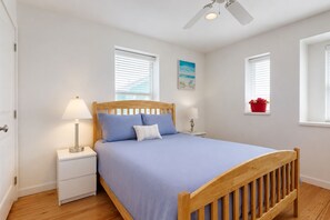 Un dormitorio con cama, mesitas de noche, ventilador de techo y ventanas.