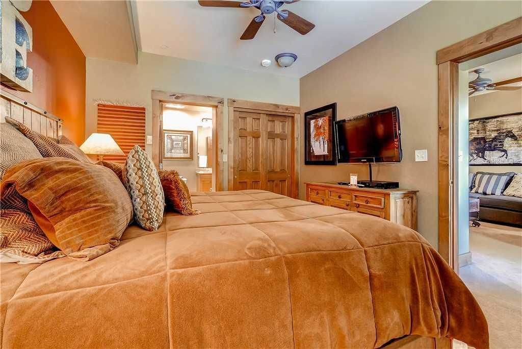 Un dormitorio con una cama grande, un ventilador de techo, un televisor y una puerta que da a otra habitación.