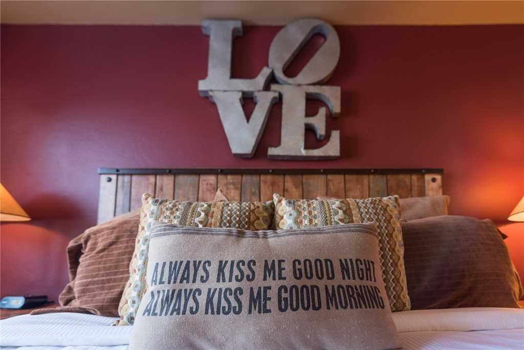 Une chambre à coucher avec un lit, des oreillers et une décoration murale sur laquelle on peut lire le mot « AMOUR ».
