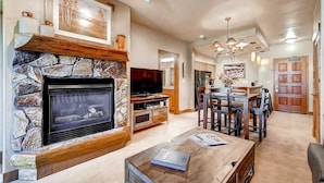 A living room with a stone fireplace, a television, and a dining area with wooden furniture. - Tl2210 Perfect for A Couple! Winter Specials!! Many Outdoor Activities! (Steamboat Springs)