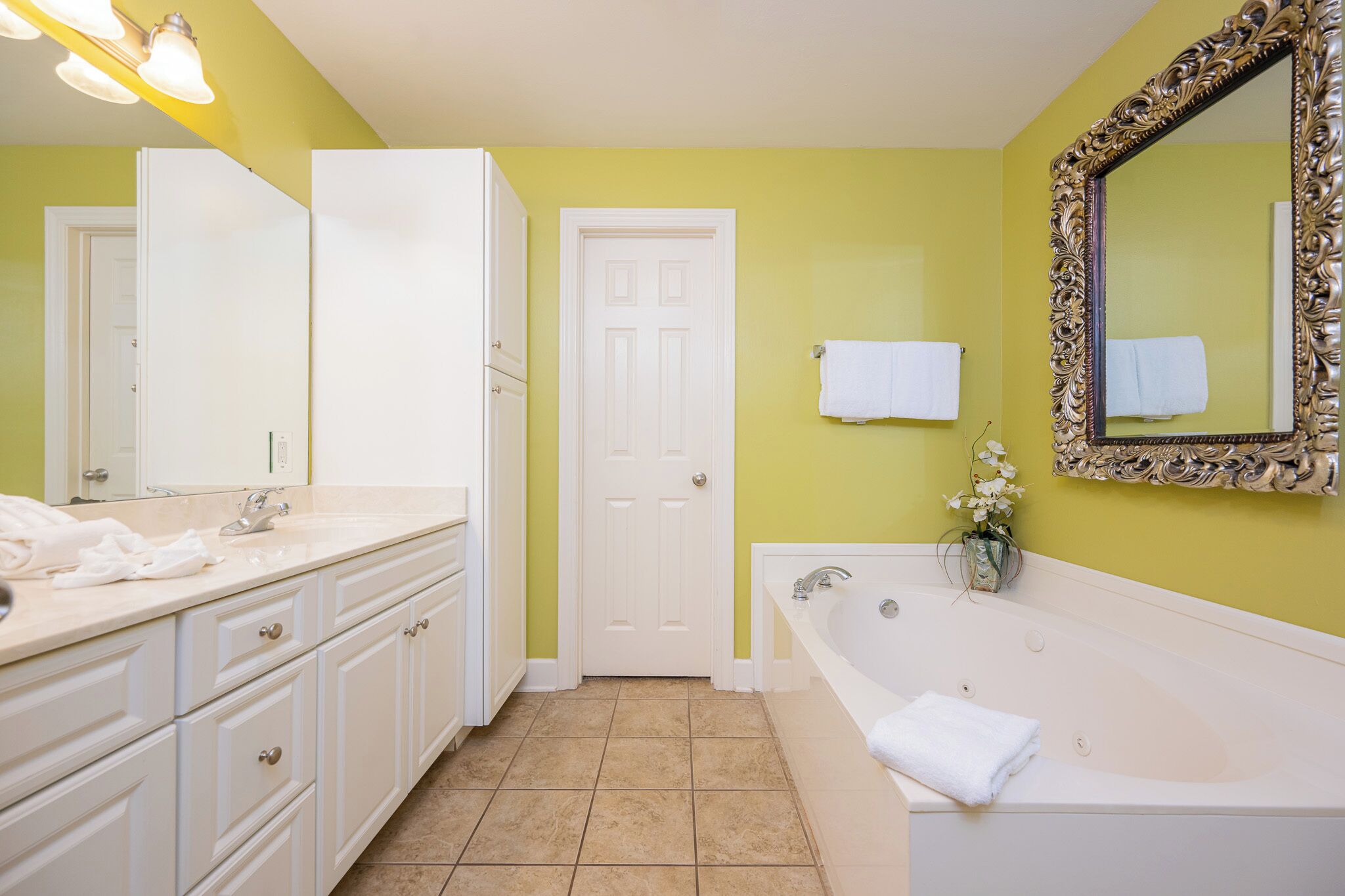 A bathroom with a white bathtub, a large mirror with an ornate frame, and a door with a towel hanging on it.